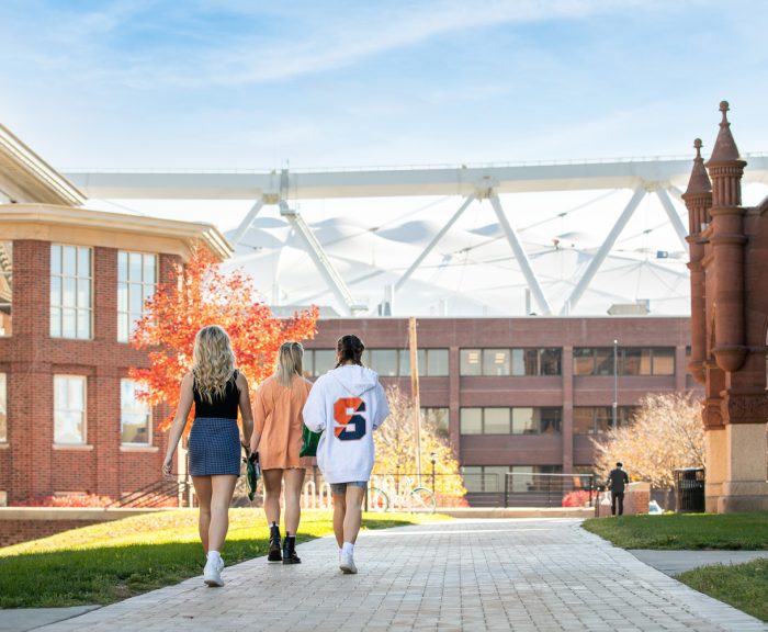 Three students walk towards the Stadium past Maxwell and Crouse College
